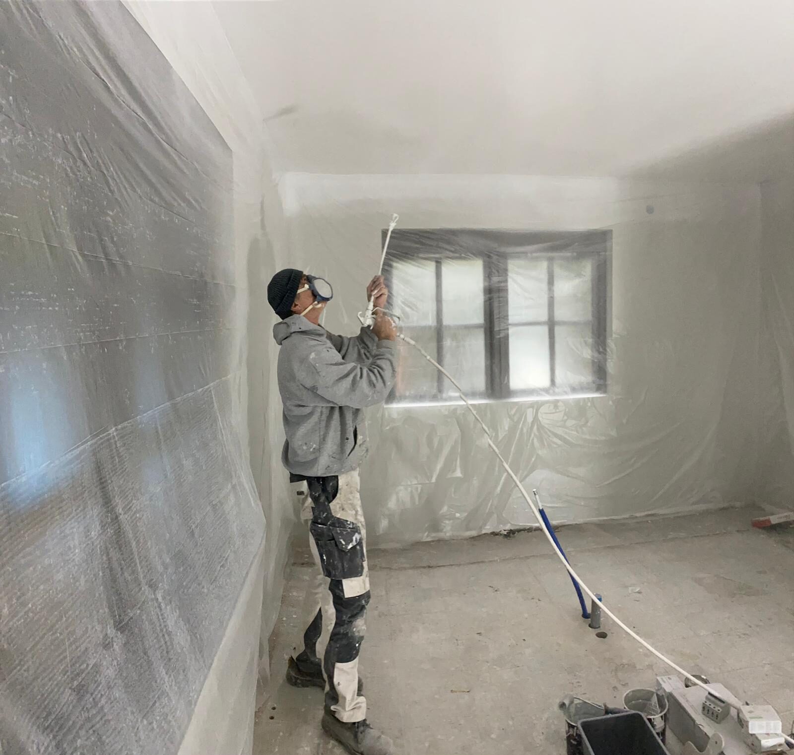 Schilder spuit latex op een plafond in een afgeplakte ruimte