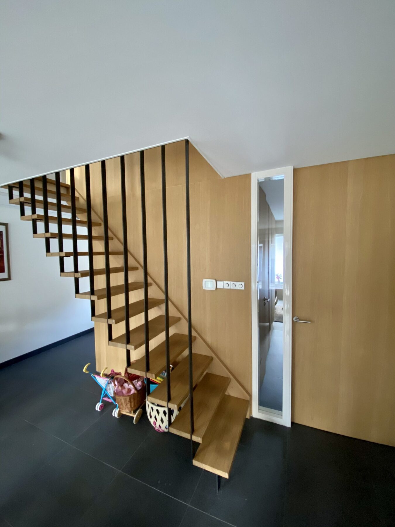 Zwevende eikenhouten trap met zwarte spijlen in een lichte hal
